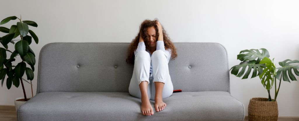 salon gris fille triste assise sur canapé et se tenant la tête