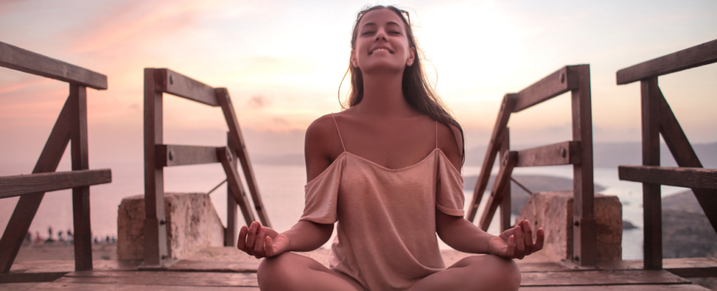 fond rose ponton bord de mer femme qui sourit et pratique la méditation mudra